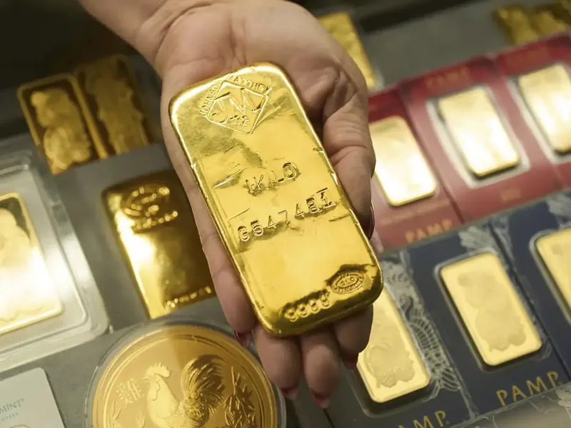 Gold bars stacked on a table with a financial chart in the background